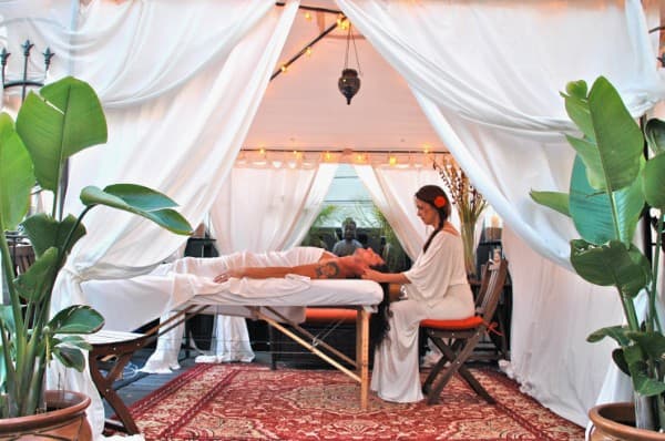 Mobile outdoor massage setup with white curtains and tropical plants